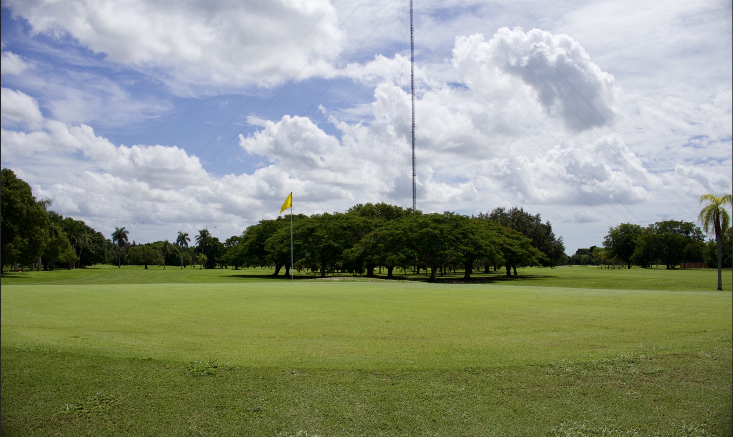 Redland Golf fairway and yellow flag beneath a wide cloud-filled sky.